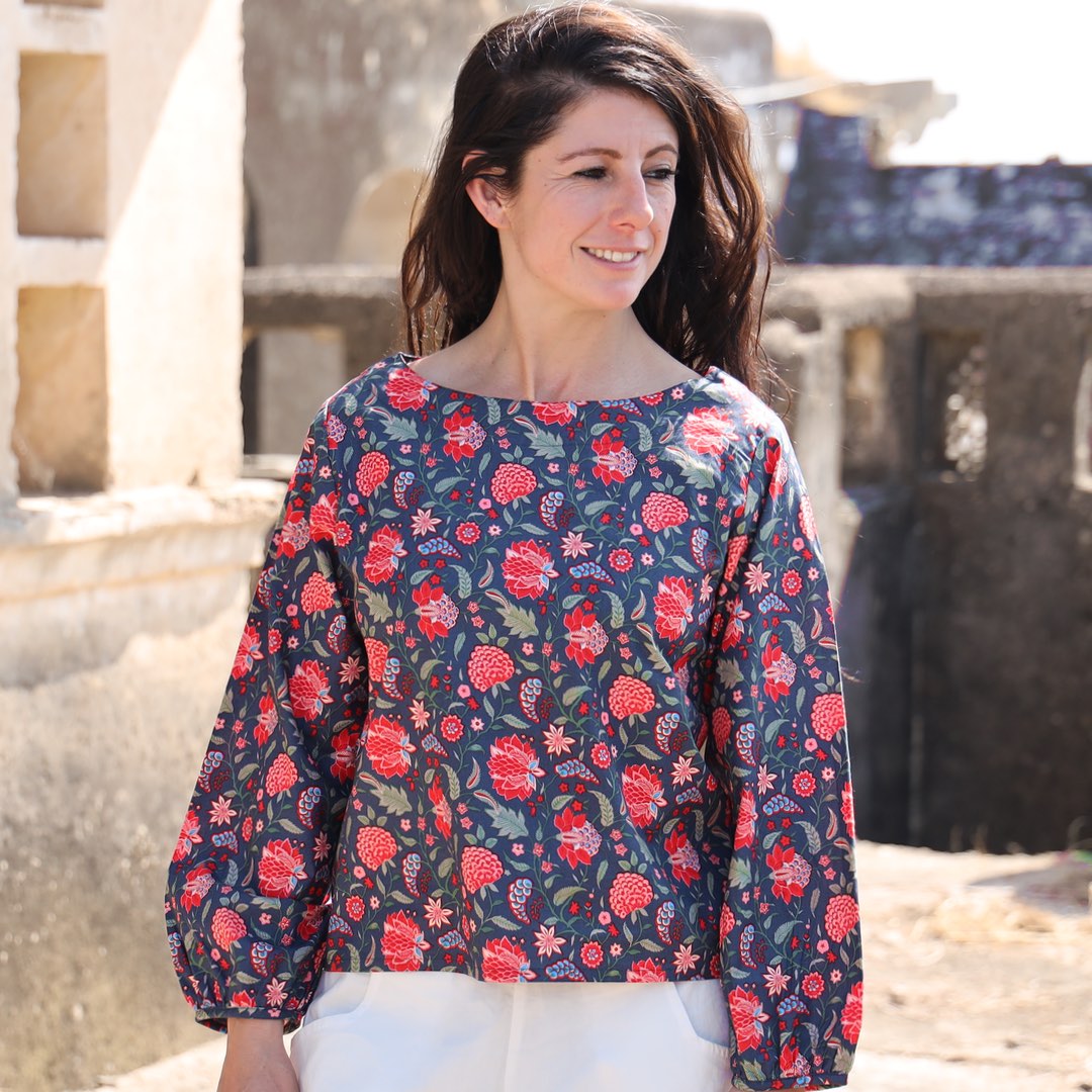woman wearing white cotton top with floral motif standing in front of blue door
