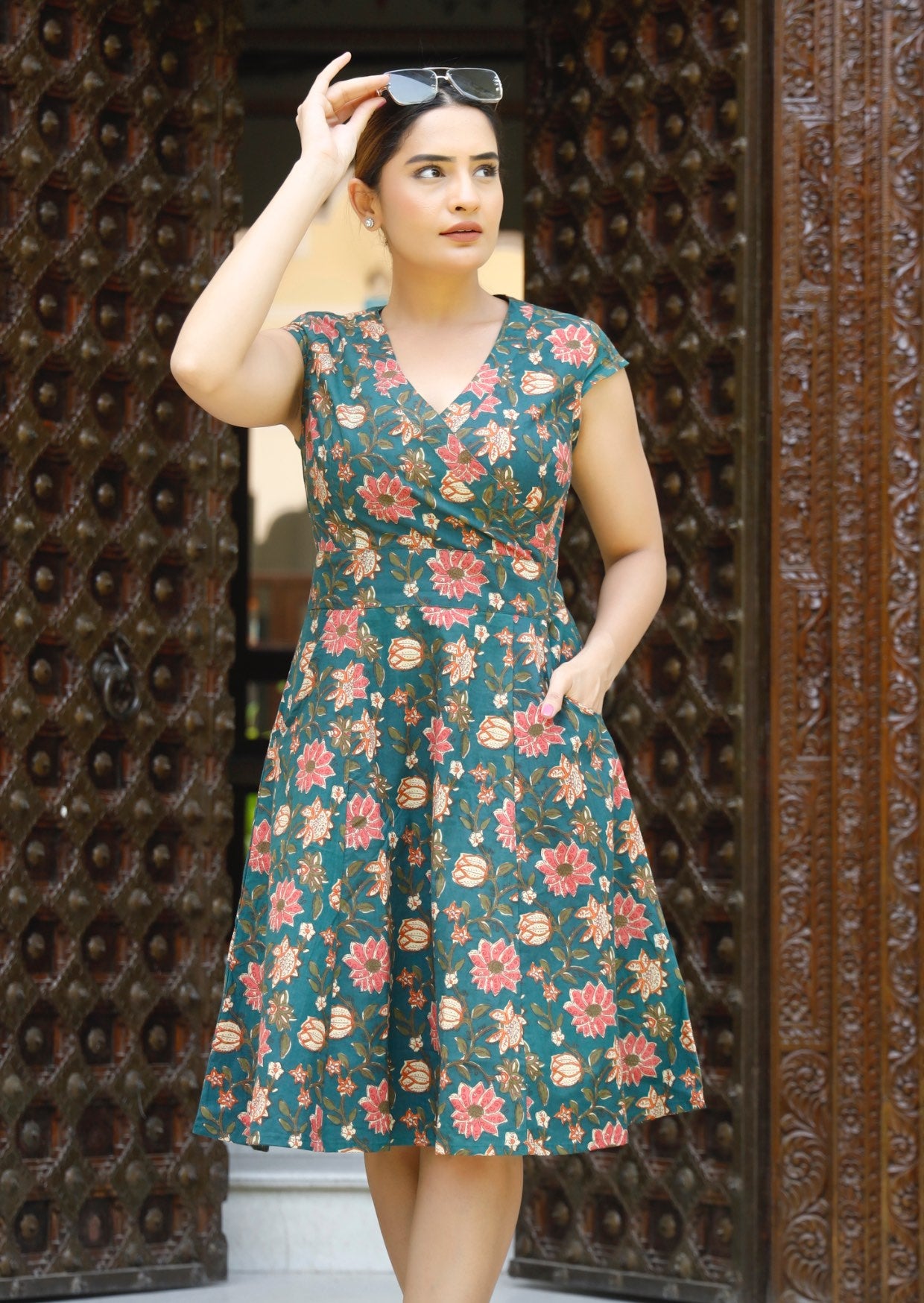 Model wears knee length cotton dress with crossover bodice, cap sleeves and generous A line skirt.