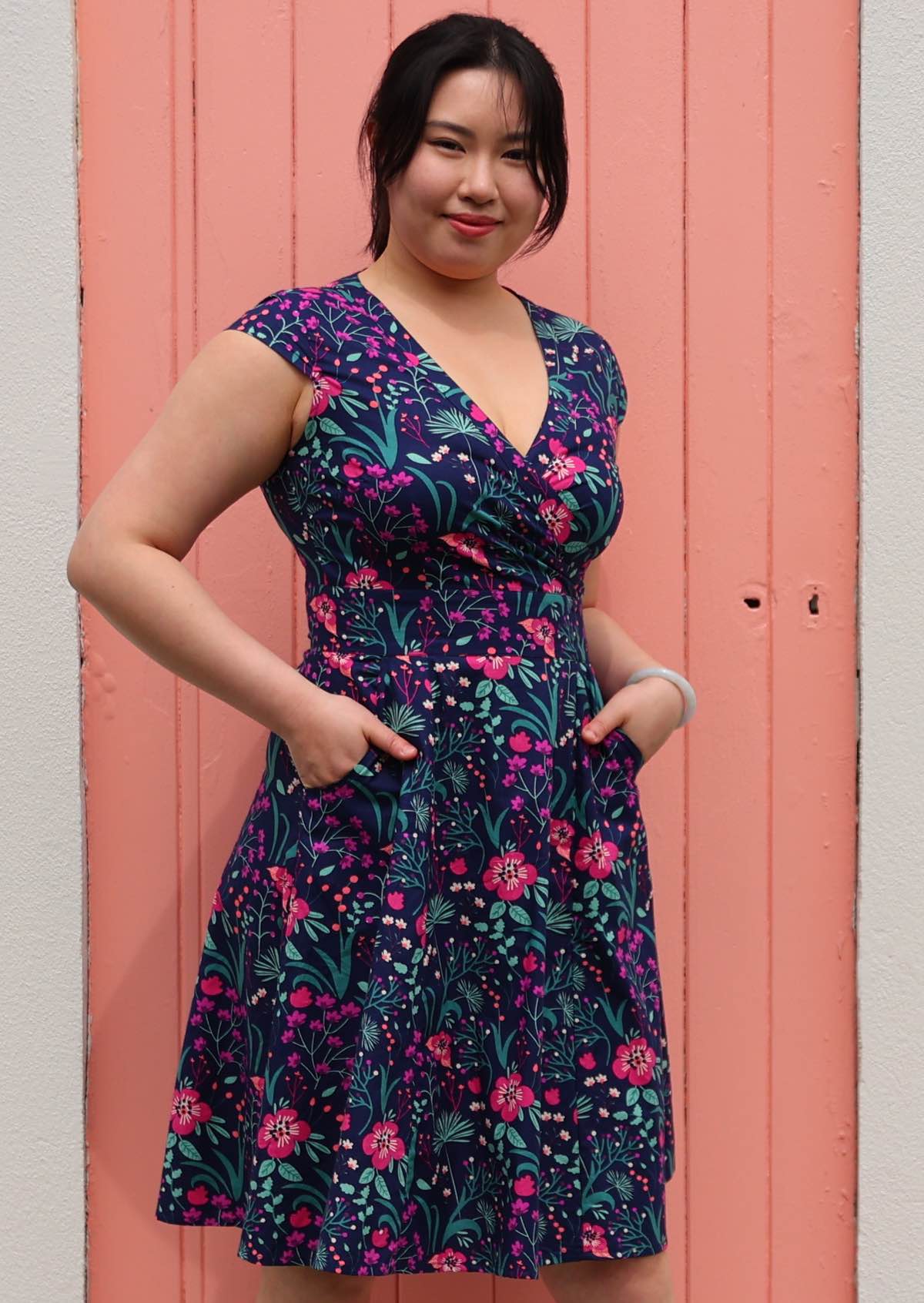 Woman in Alice Dress Dianthus retro style 100% cotton navy blue floral with cross over bodice and pockets fit and flare style dress hands in pockets