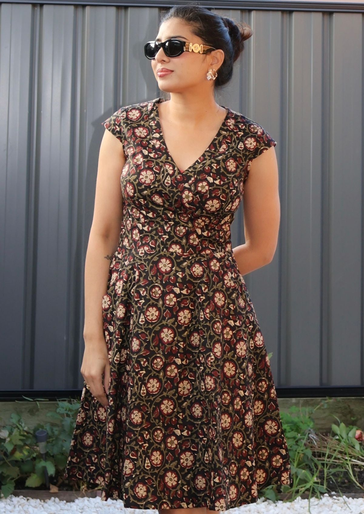 Woman wearing a floral dress with sunglasses against a gray wall.