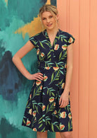 Model wears navy based dress with green floral pattern. 
