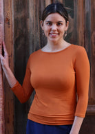 Woman wearing a rayon boat neck orange 3/4 sleeve top with navy pants.