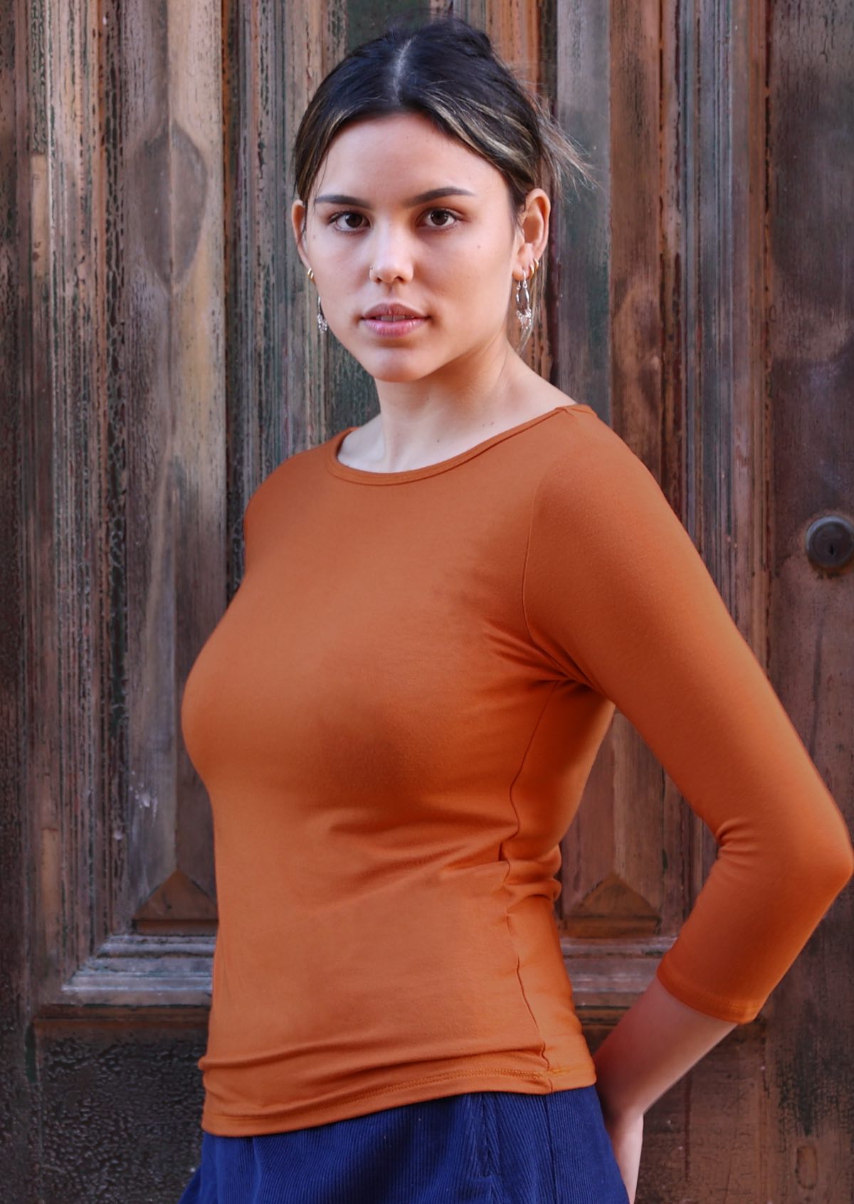 Woman with dark hair wearing a rayon boat neck orange 3/4 sleeve top.