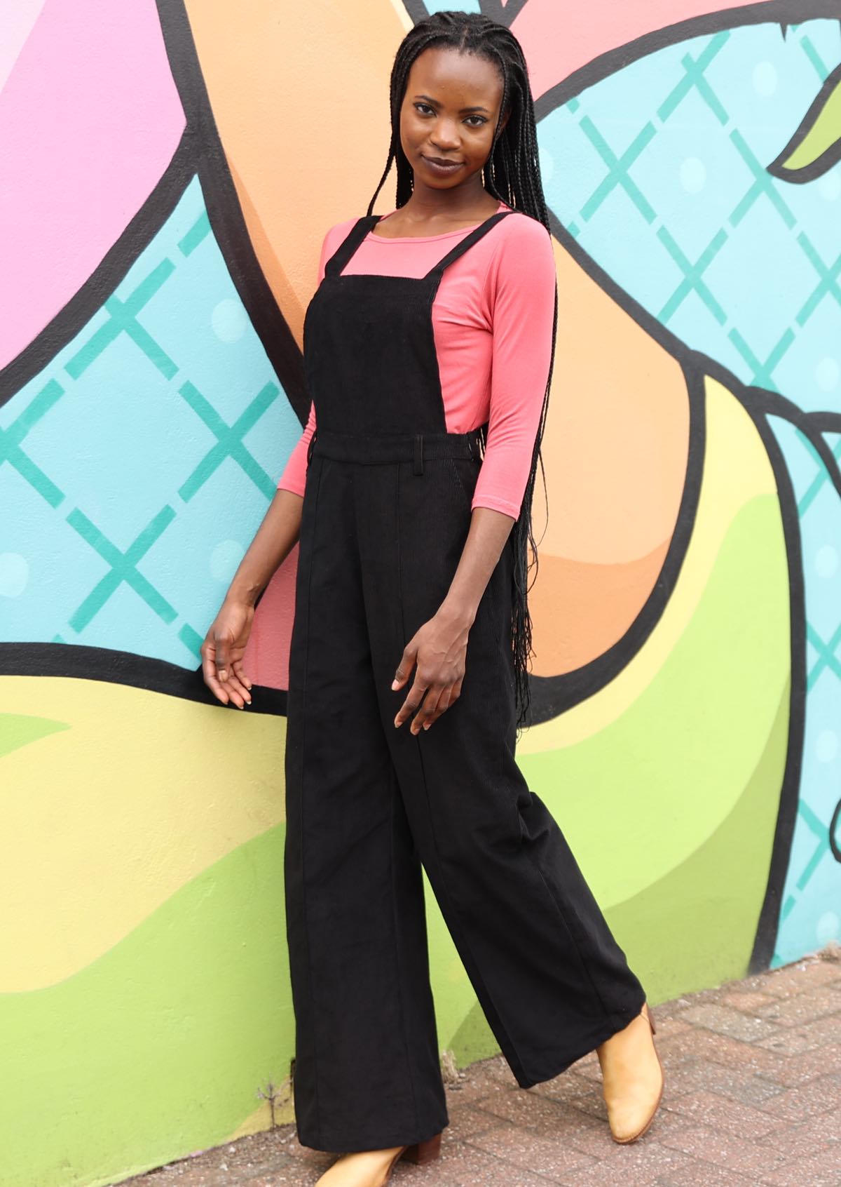 Woman wearing 100% cotton corduroy overalls in black over pink long sleeve top