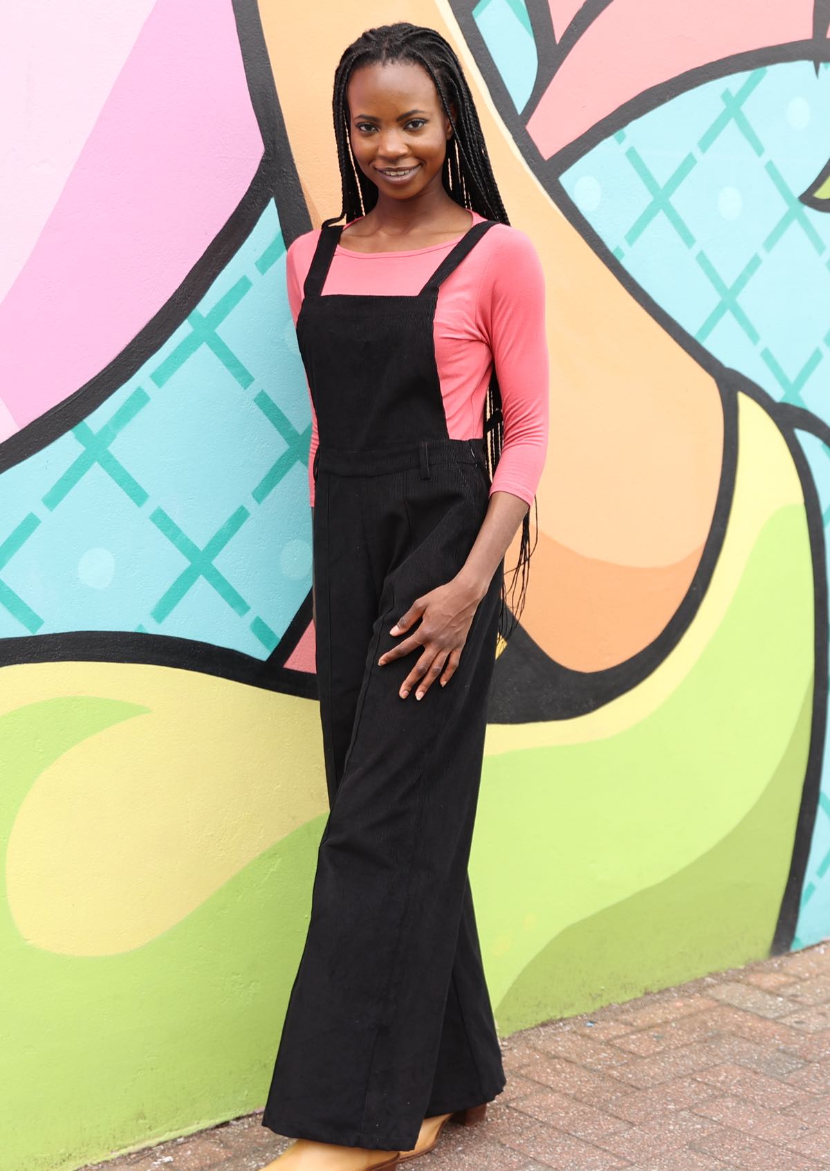 Woman wearing 100% cotton corduroy overalls in black with pink top underneath