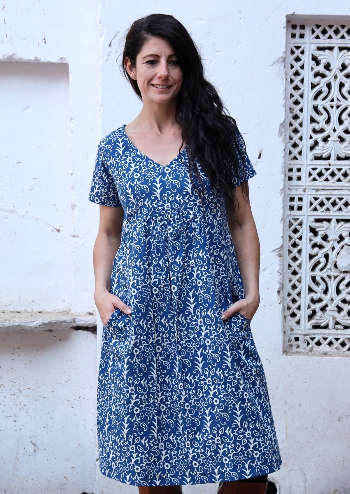 Woman stands in cotton short sleeve dress in gorgeous white floral print on a blue base, with her ands in pockets