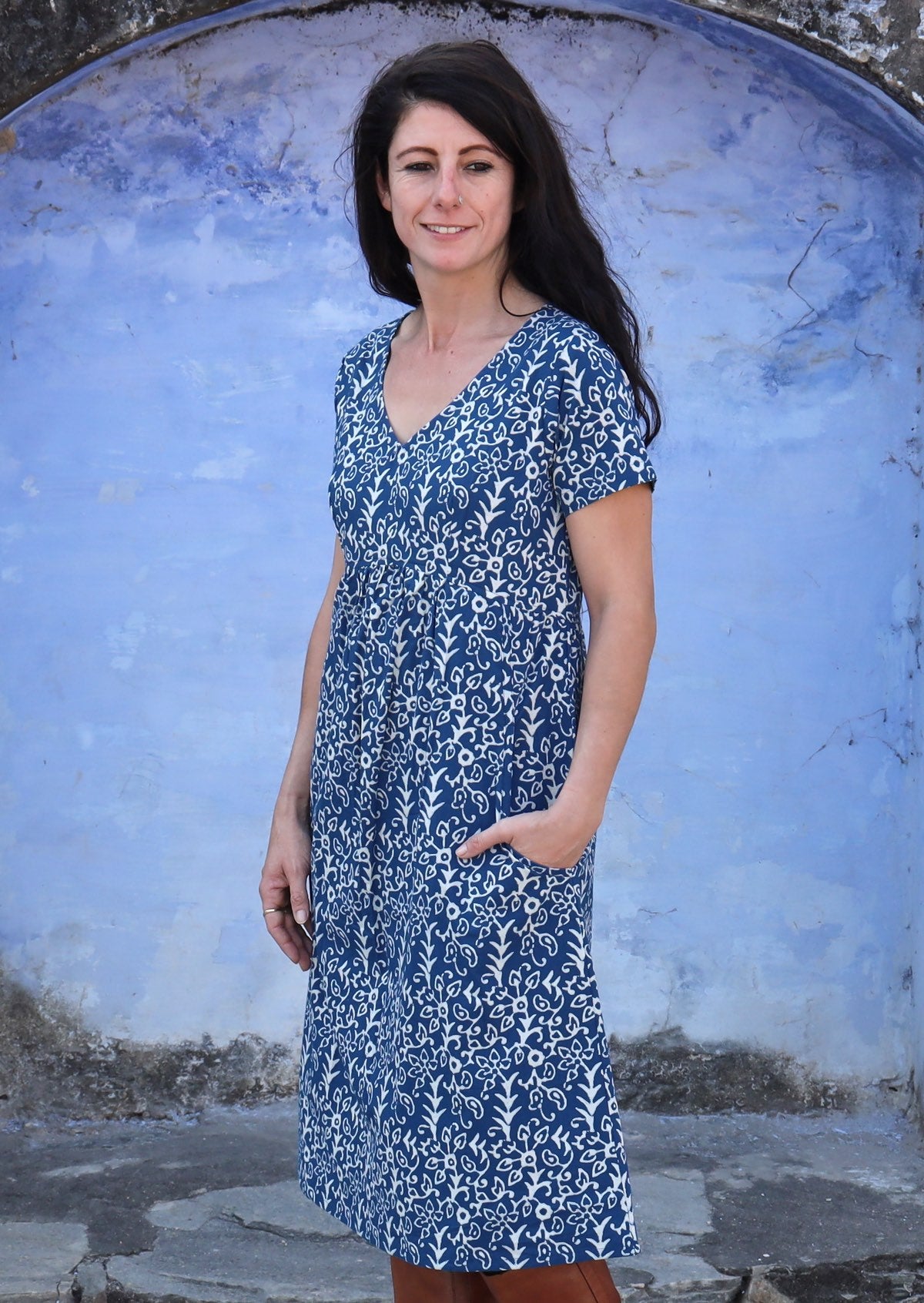 Woman stands sideways in cotton over the knee length relaxed fit dress with short sleeves and an empire waistline