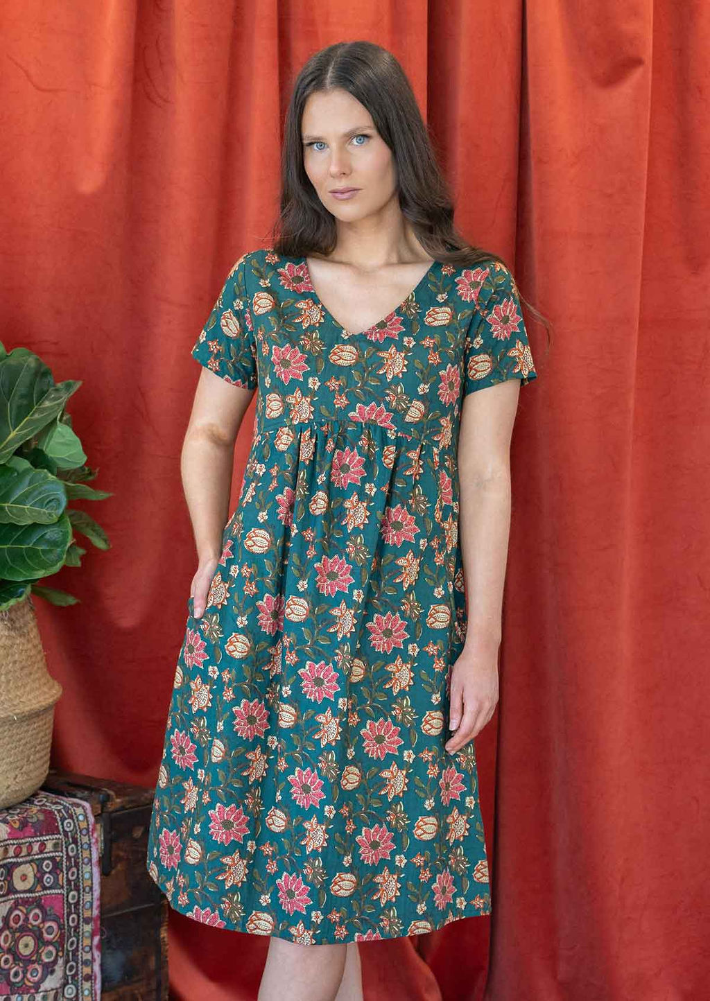 Model wearing a cotton V-neck short sleeve dress with empire waistline and hand in pocket.