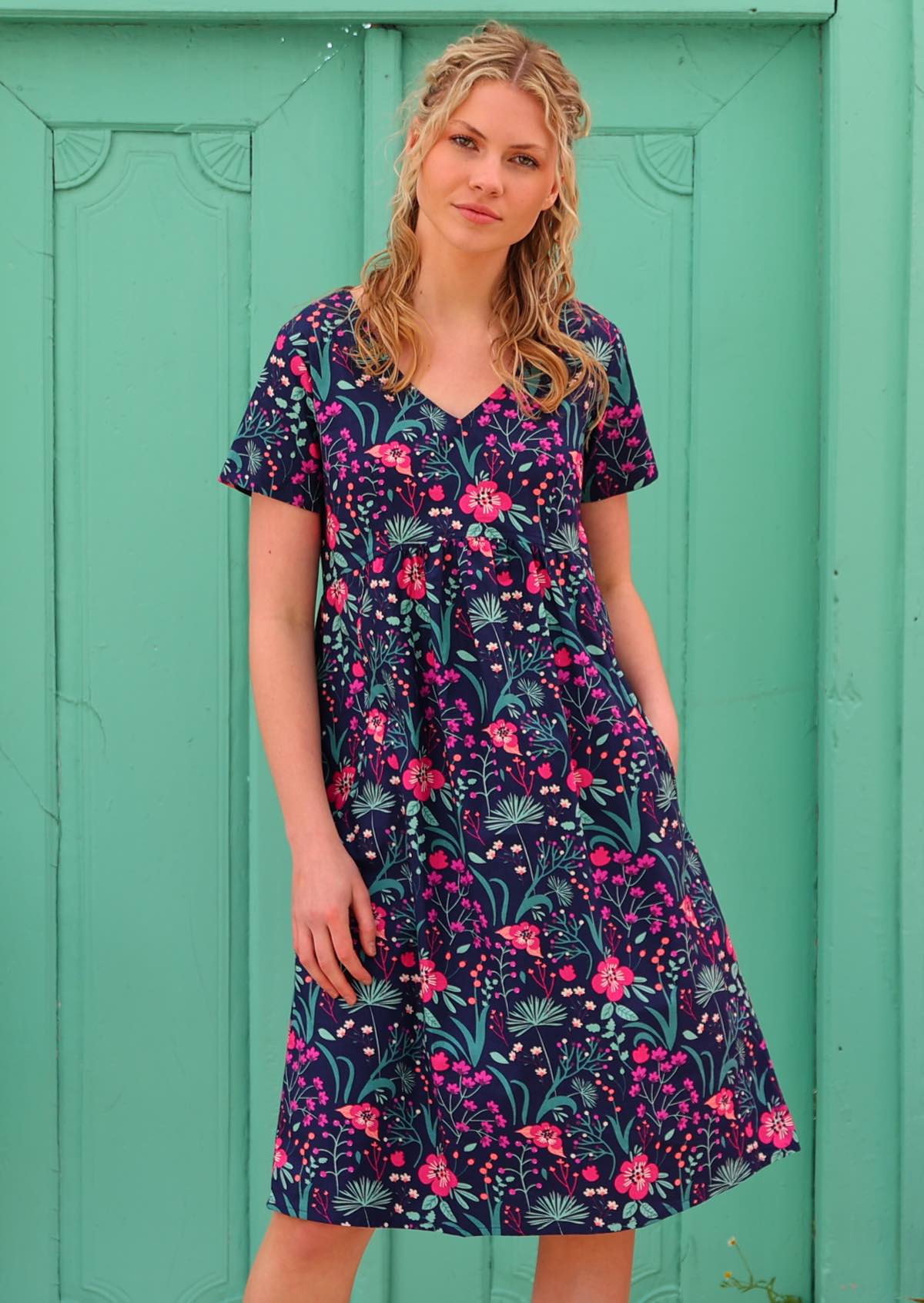 Model wearing 100 percent cotton v-neck sundress with hot pink and bright purple flowers on a deep blue base, with pockets
