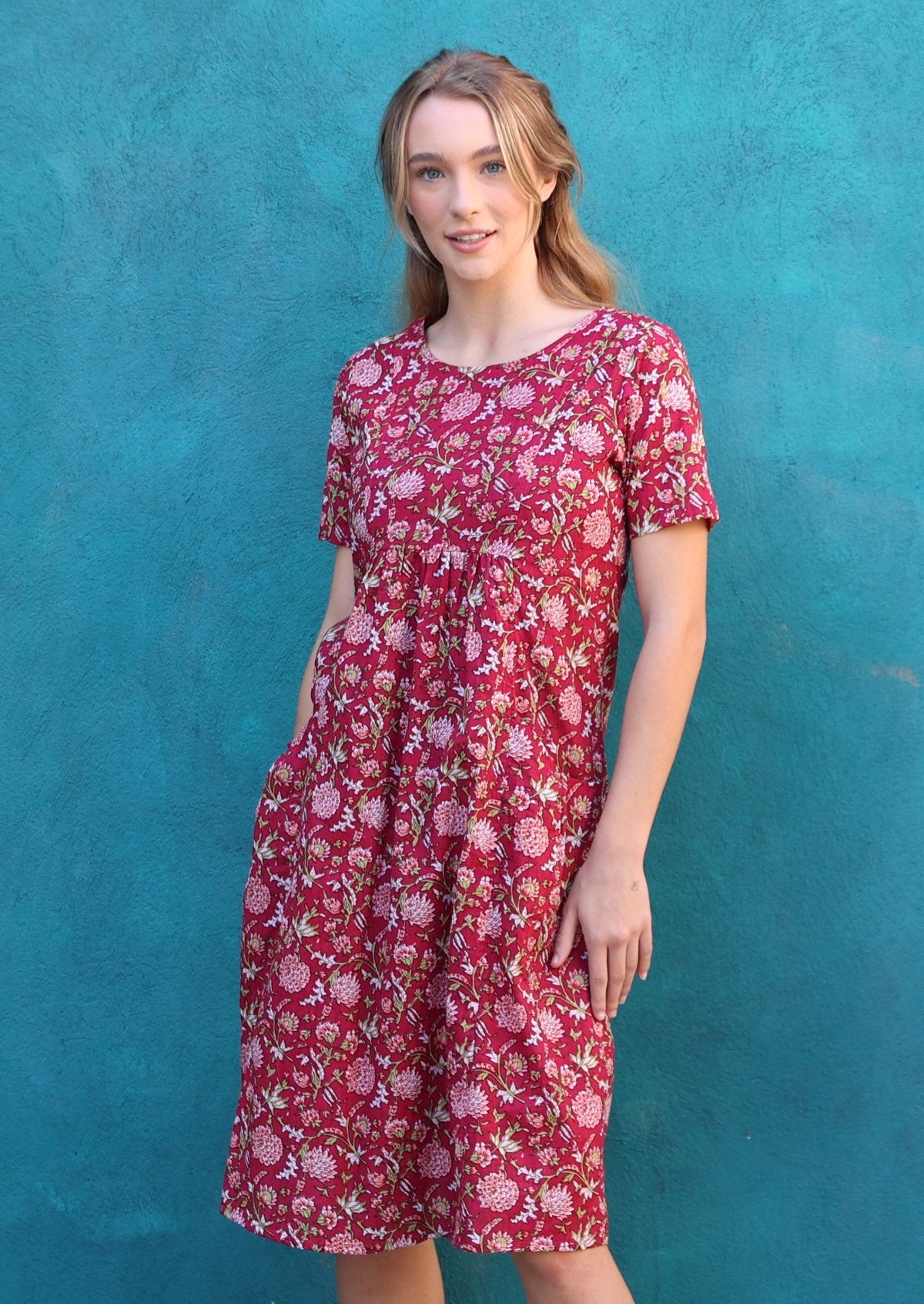 Woman wears sweet floral print on cranberry base cotton sun dress with short sleeves and a round neckline