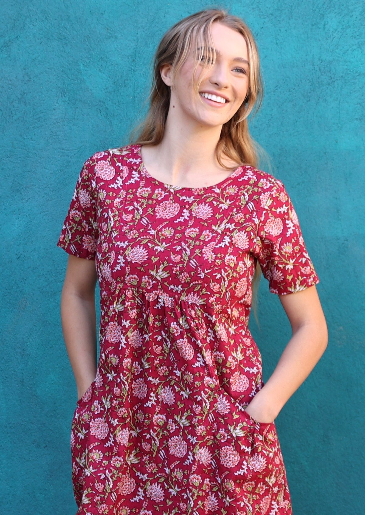 Close up of woman in cranberry based floral print cotton short sleeve dress with her hands in the deep pockets