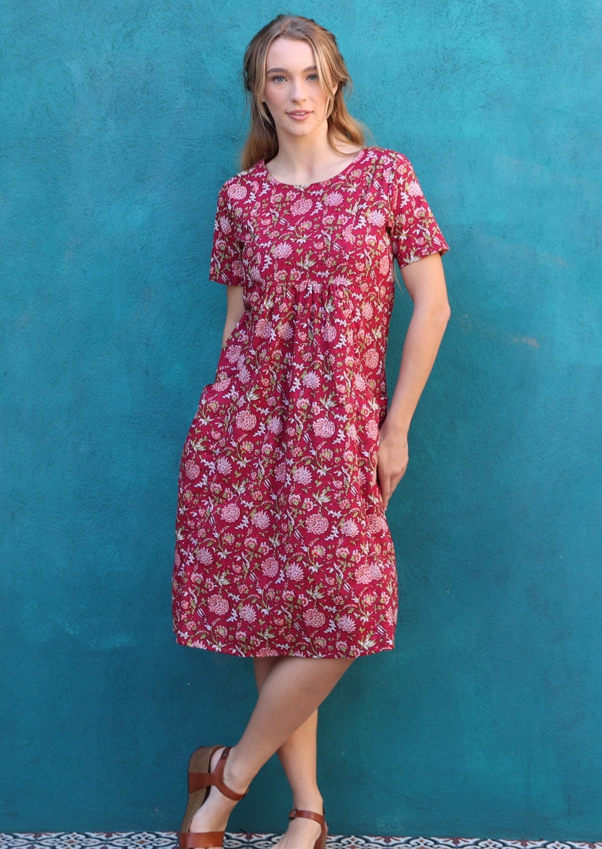 Model poses in cotton short sleeve below knee length cotton dress with small gathers under the bust and a round neckline