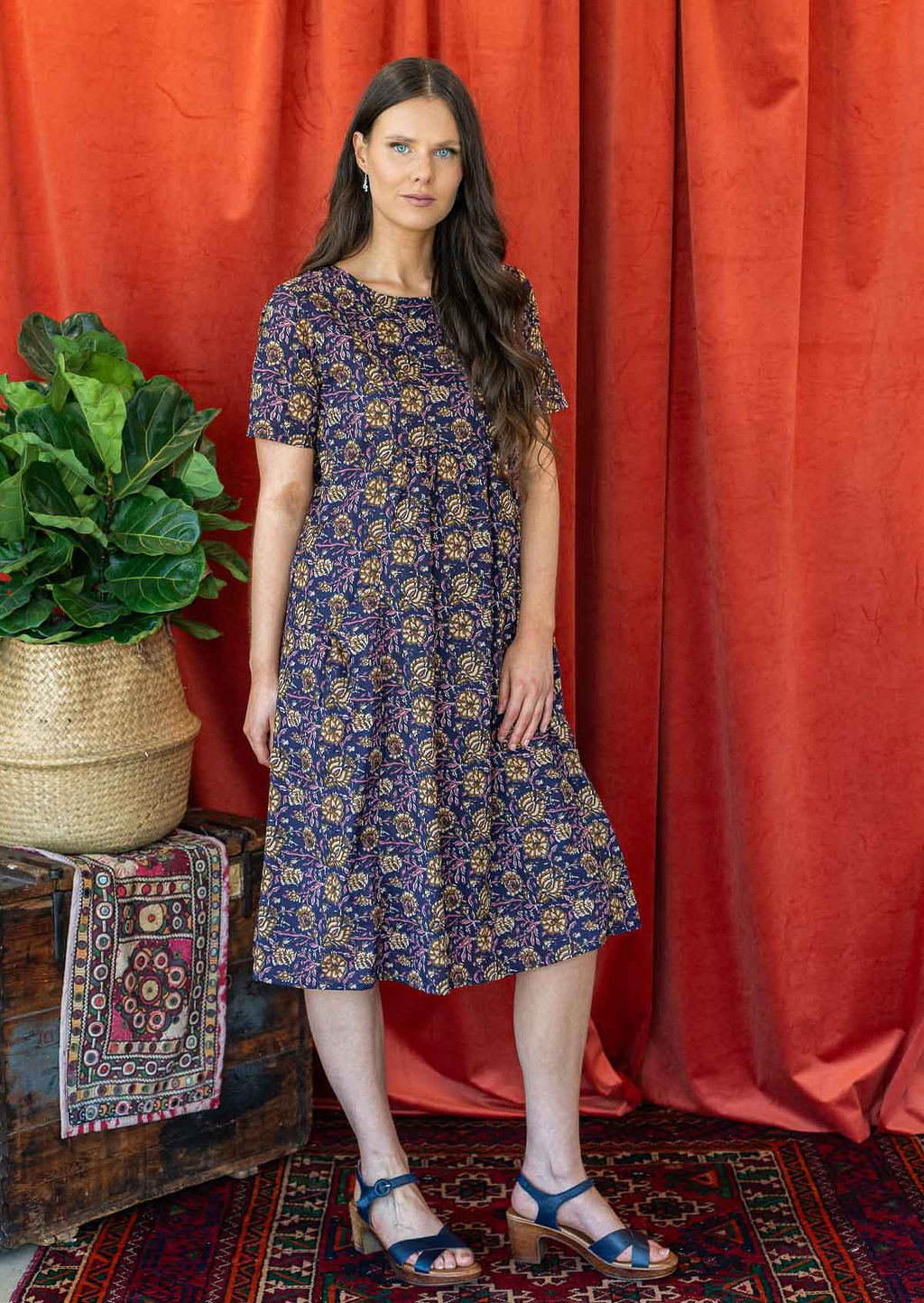 Model wears dark purple based floral printed cotton dress with short sleeves and a round neckline.