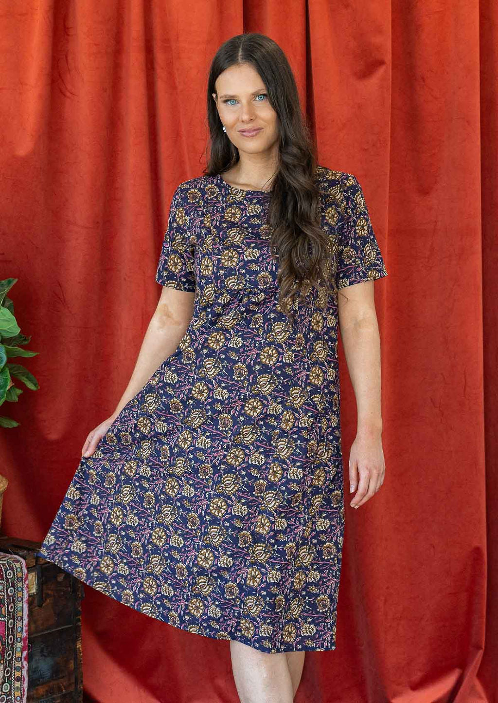 Model wearing over the knee length cotton dress with round neckline, short sleeves and gathers under the bust.