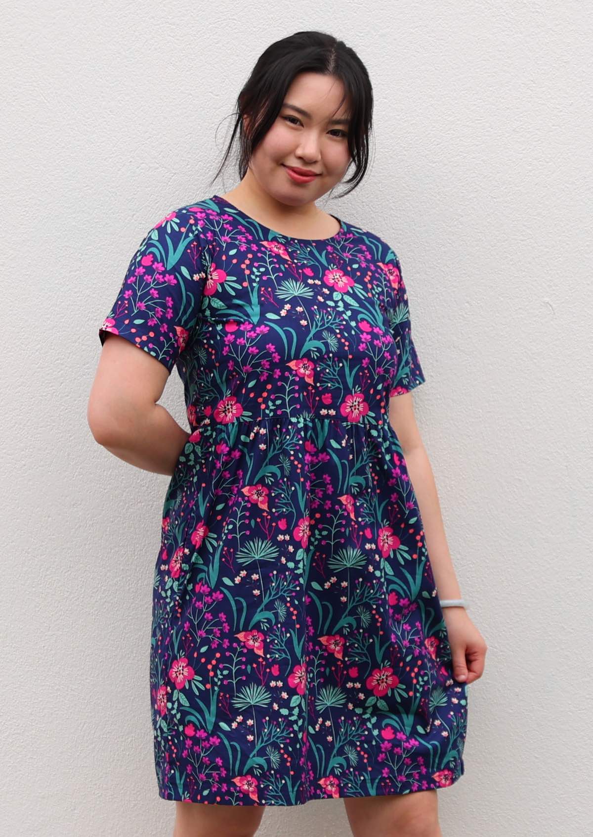 woman in loose fit purple, navy and pink floral print 100% cotton dress in front of hands behind back