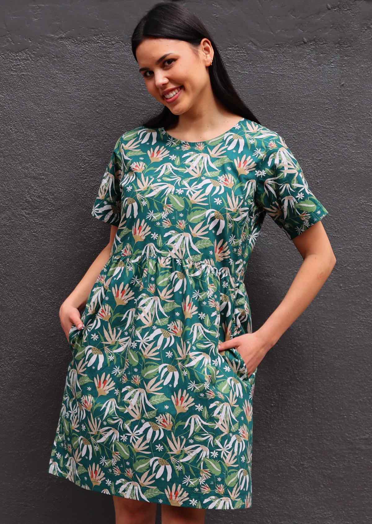 Model with dark hair in loose fit green cotton floral dress with hands in pockets