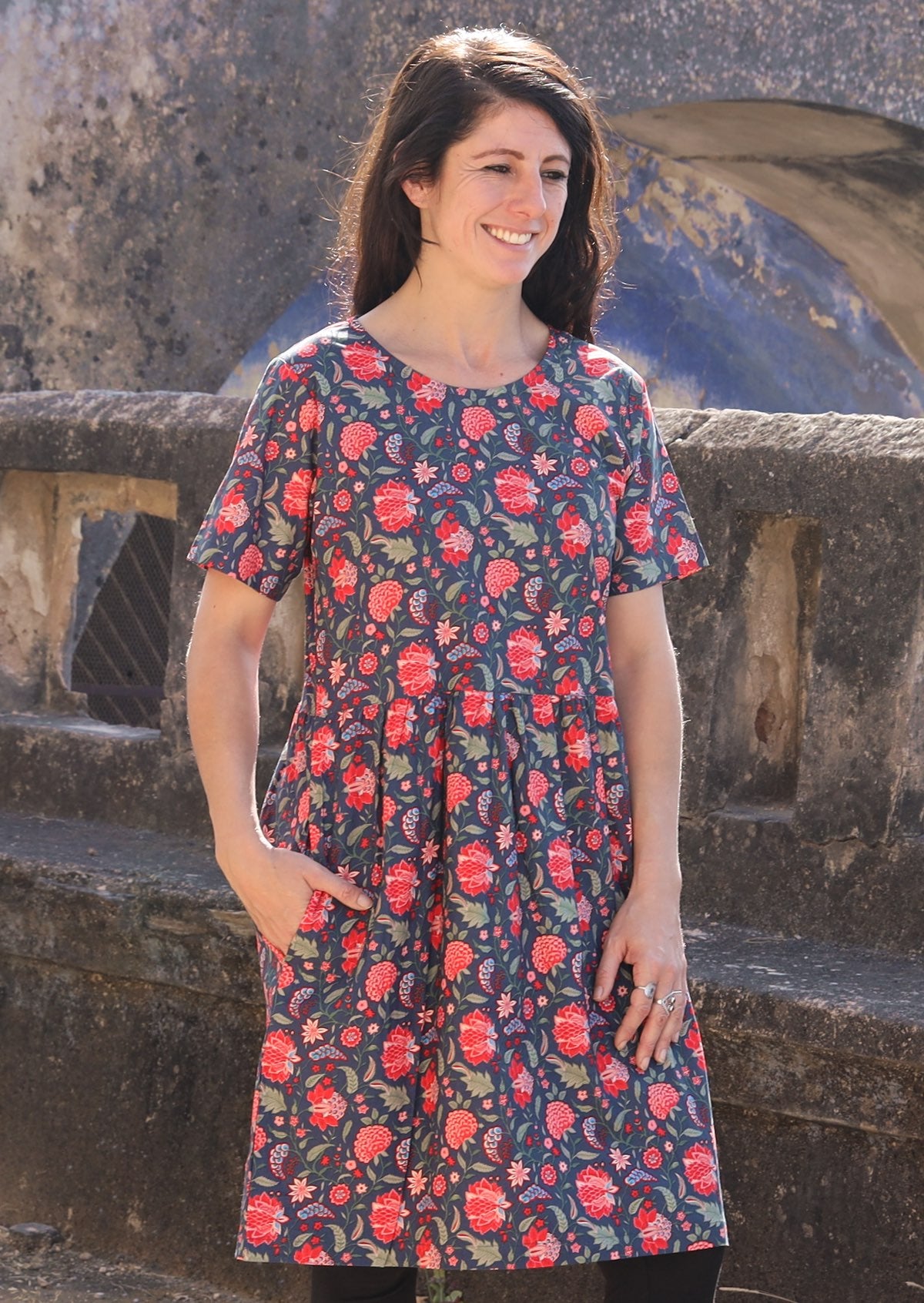 Woman looking to the side wearing 100 percent cotton blue base retro dress with leaf and floral print with one hand in pocket