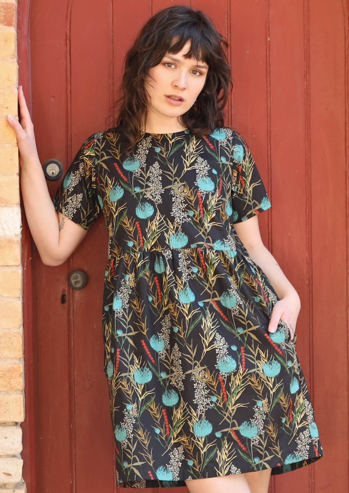 Model wearing black base cotton with botanical print, high round neckline, t-shirt sleeves, an empire waistline and hidden side pockets 