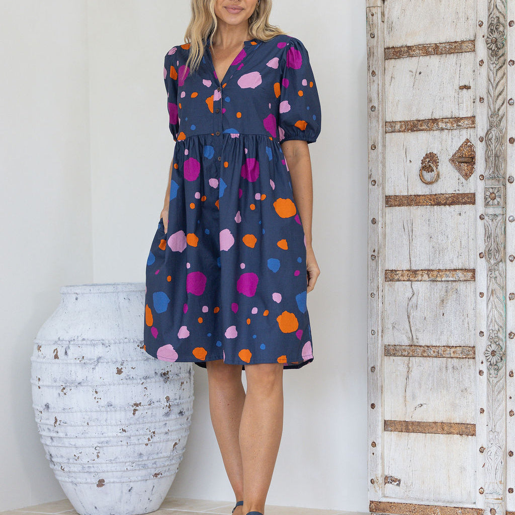 Woman wearing a colourful polka dot on a blue base cotton button through babydoll dress