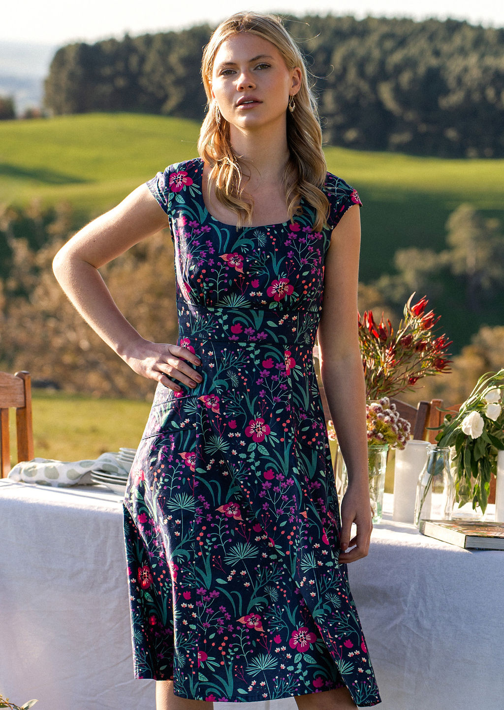 woman in retro inspired Scarlett Dress Dianthus in a vibrant navy, purple, pink and aqua floral print on 100% cotton in country setting