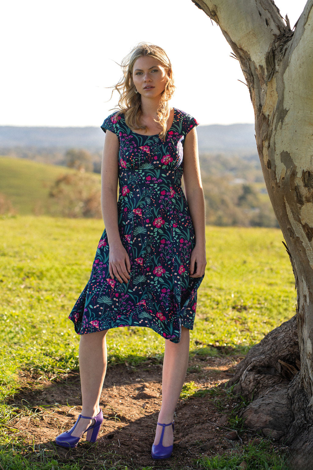 woman in retro inspired Scarlett Dress Dianthus in a vibrant navy, purple, pink and aqua floral print on 100% cotton under gum tree