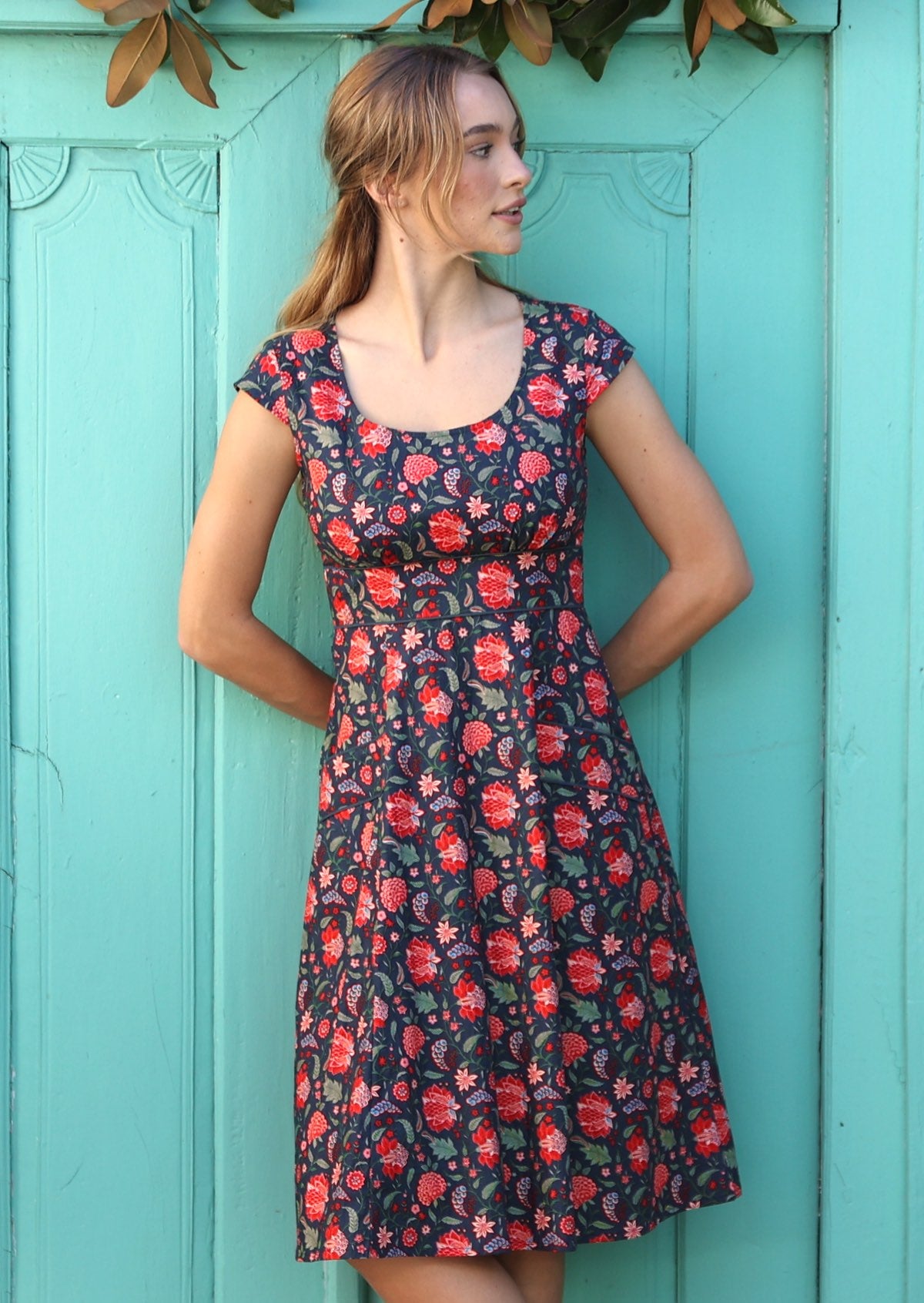 Model is wearing a bright floral printed blue dress with scoop neck and wide waistband .
