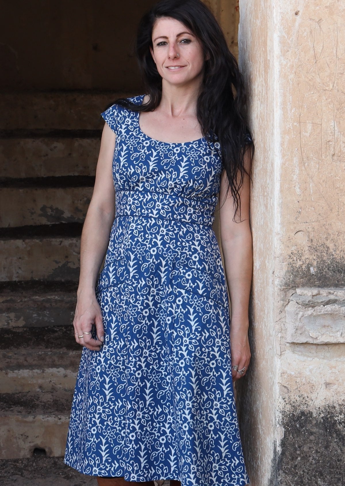 Model with blue 100 percent cotton scoop neck retro dress with pockets leaning against a wall