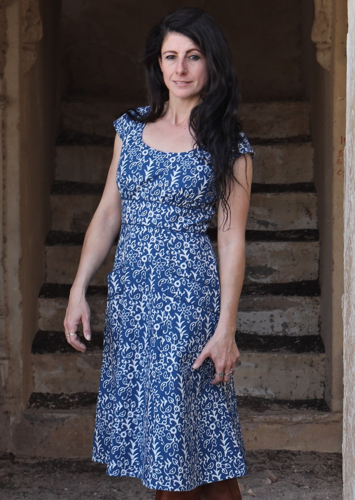 Model standing in front of stairs wearing blue 100 percent cotton scoop neck retro dress with pockets