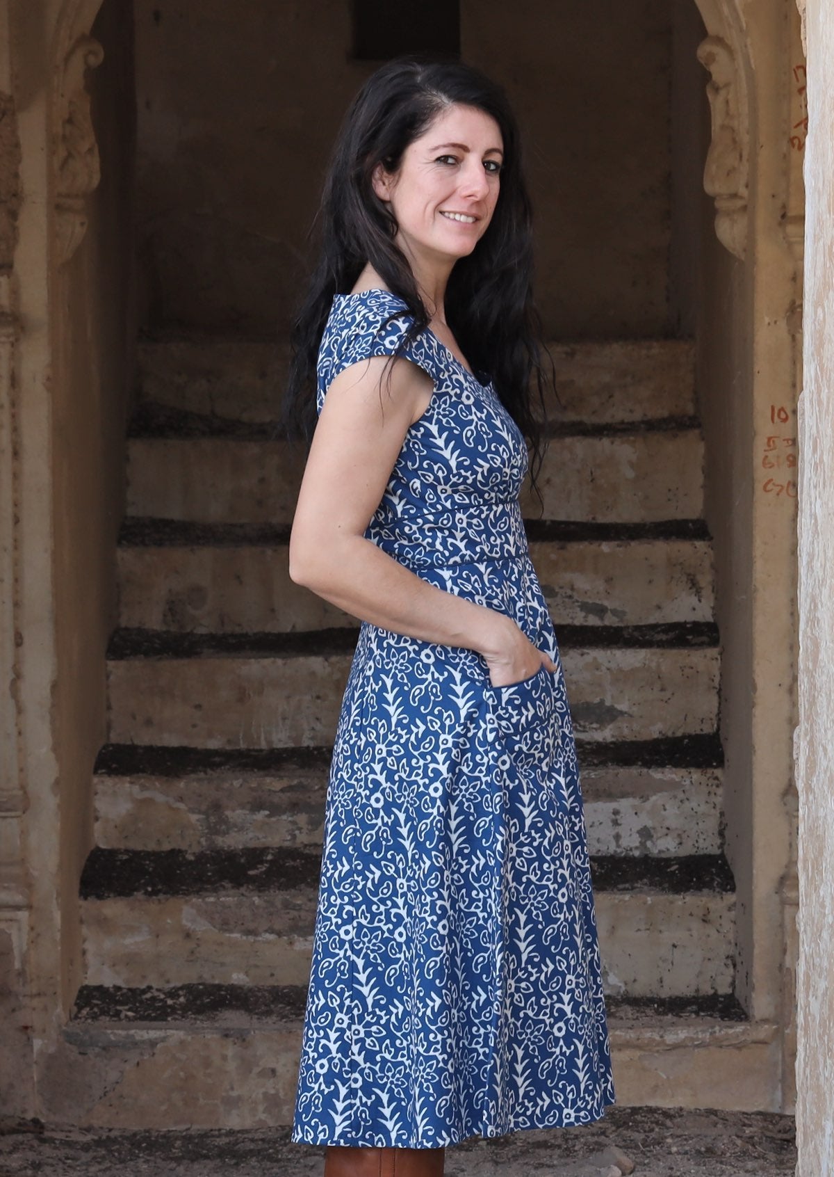 Model standing side on wearing blue 100 percent cotton scoop neck retro dress with hand in pocket