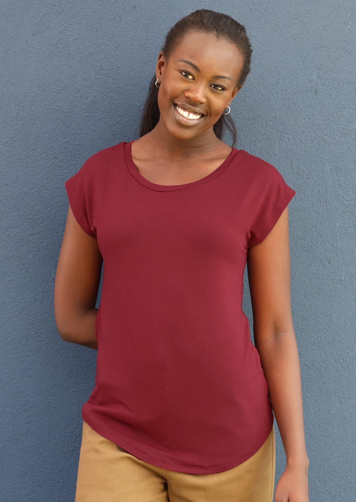 Woman with black hair wearing a soft flattering fit maroon rayon jersey t-shirt in front of grey wall.