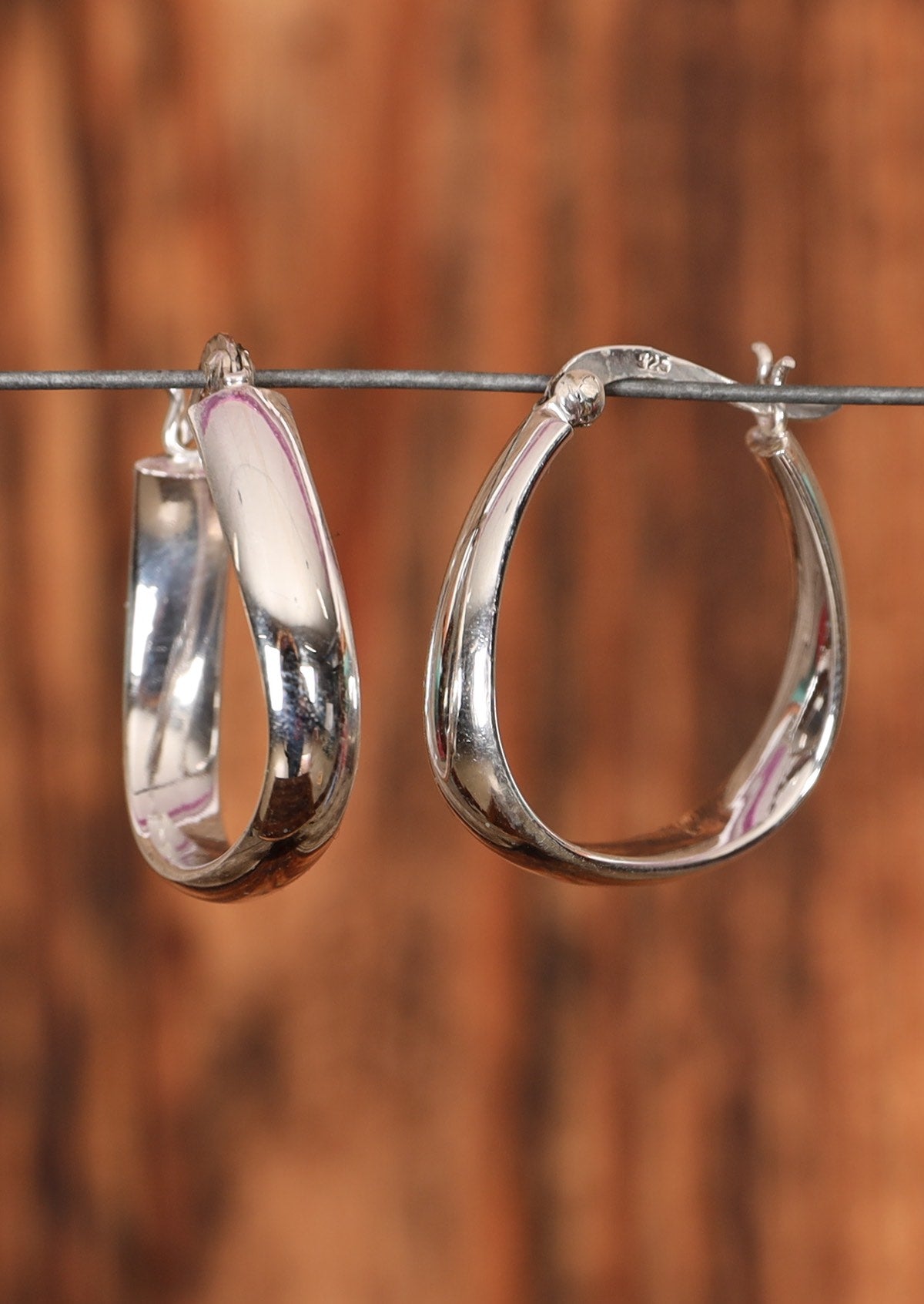 92.5% silver petite abstract hoop earrings placed on a wire for display.