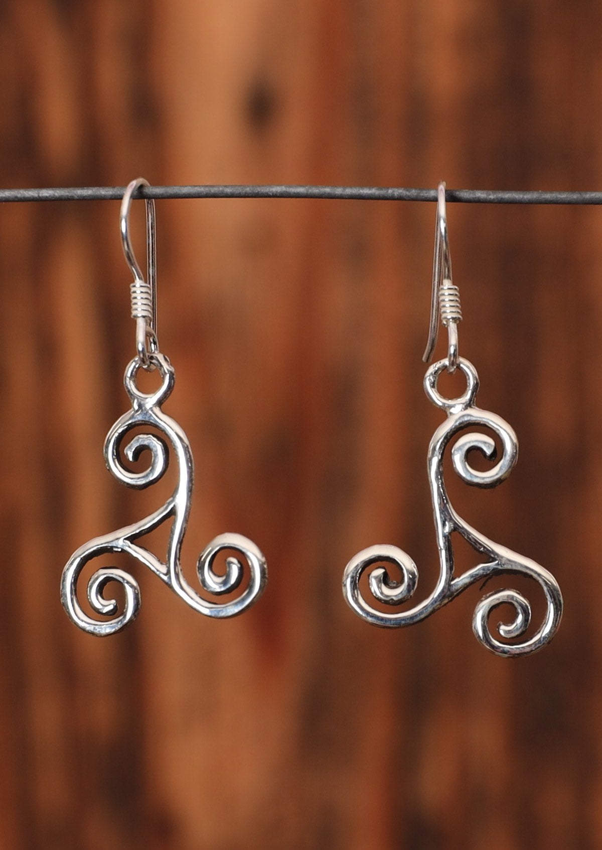 92.5% silver sleek Triskele earrings sit on a wire for display.