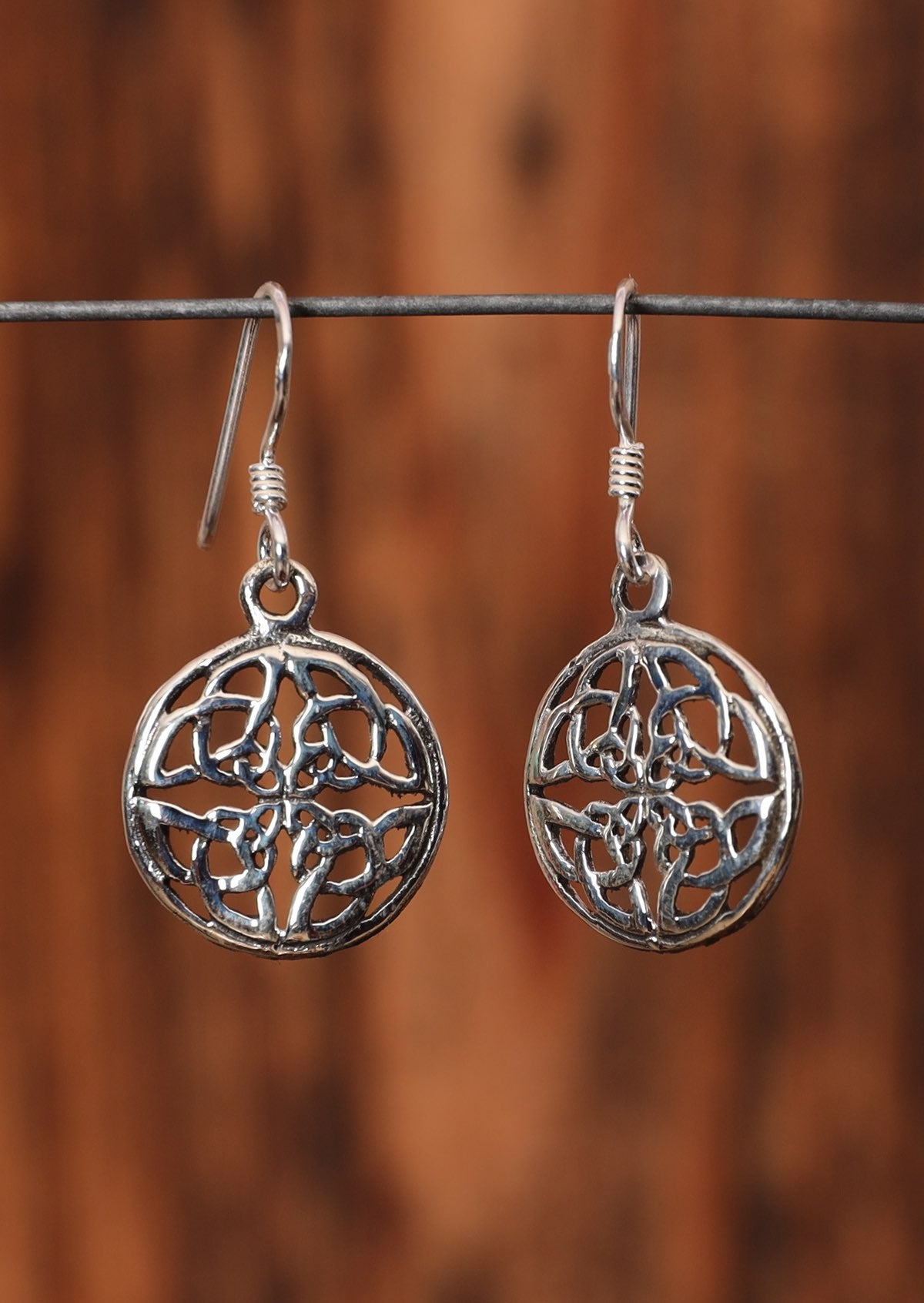 92.5% silver Celtic style woven medallion earrings sit on a wire for display.