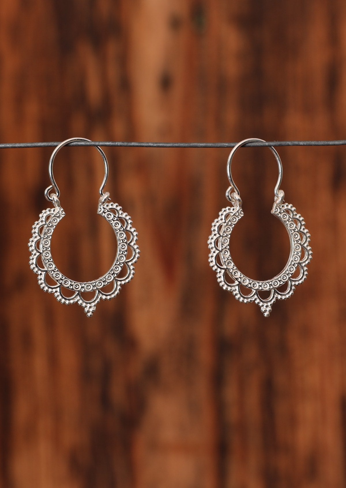 92.5% silver lace style hoop earrings sit on a wire for display.