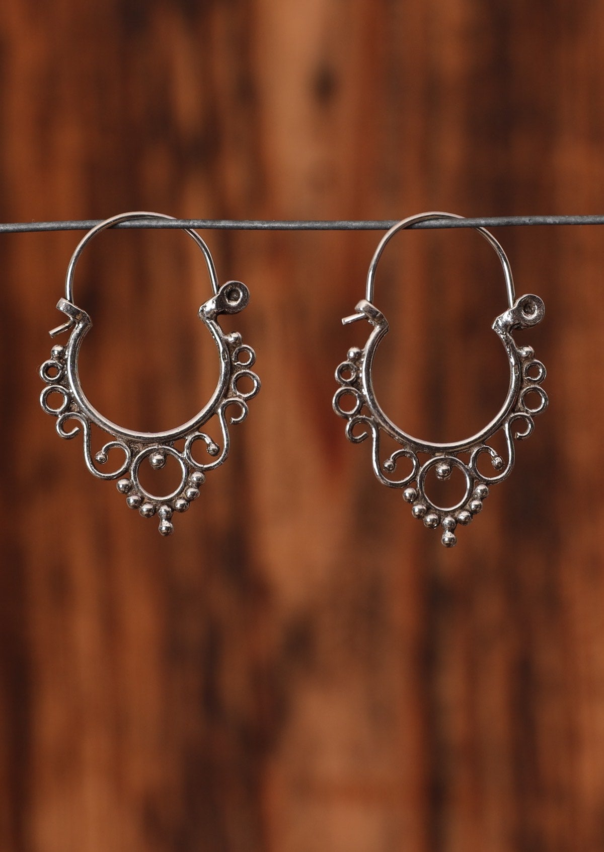 92.5% silver ornate curved earring sitting on a wire for display.