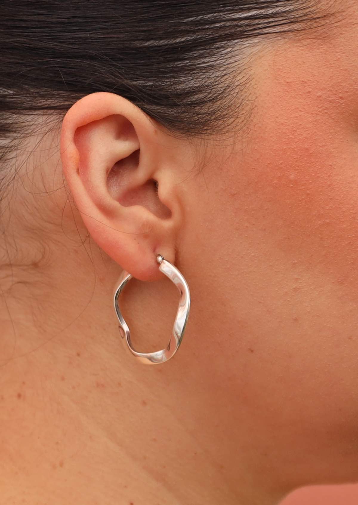 Waving sterling silver hoop earrings on woman's ear