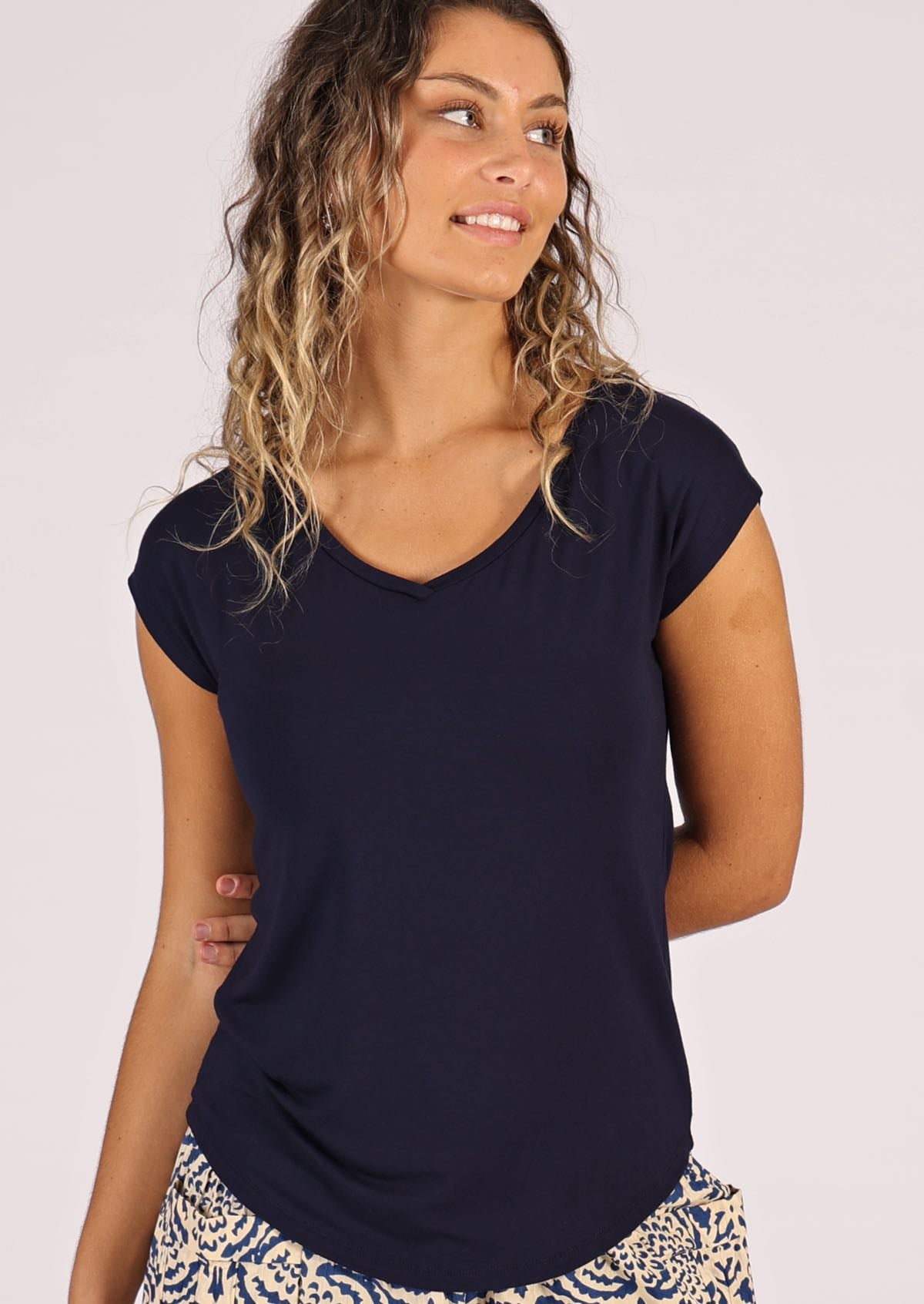 Woman with blonde hair looking to the side wearing a navy blue v-neck short cap sleeve rayon top