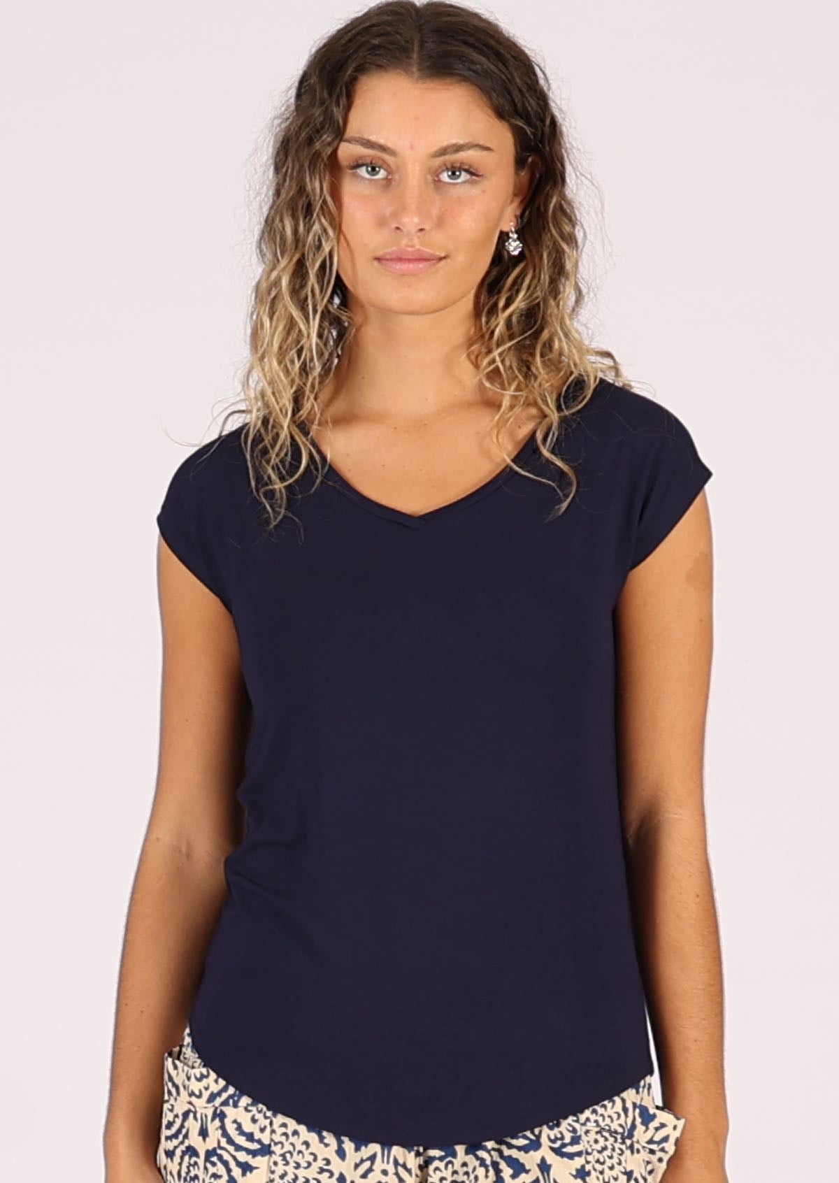 Woman wearing a navy blue v-neck short cap sleeve rayon top with floral cream and blue pants.