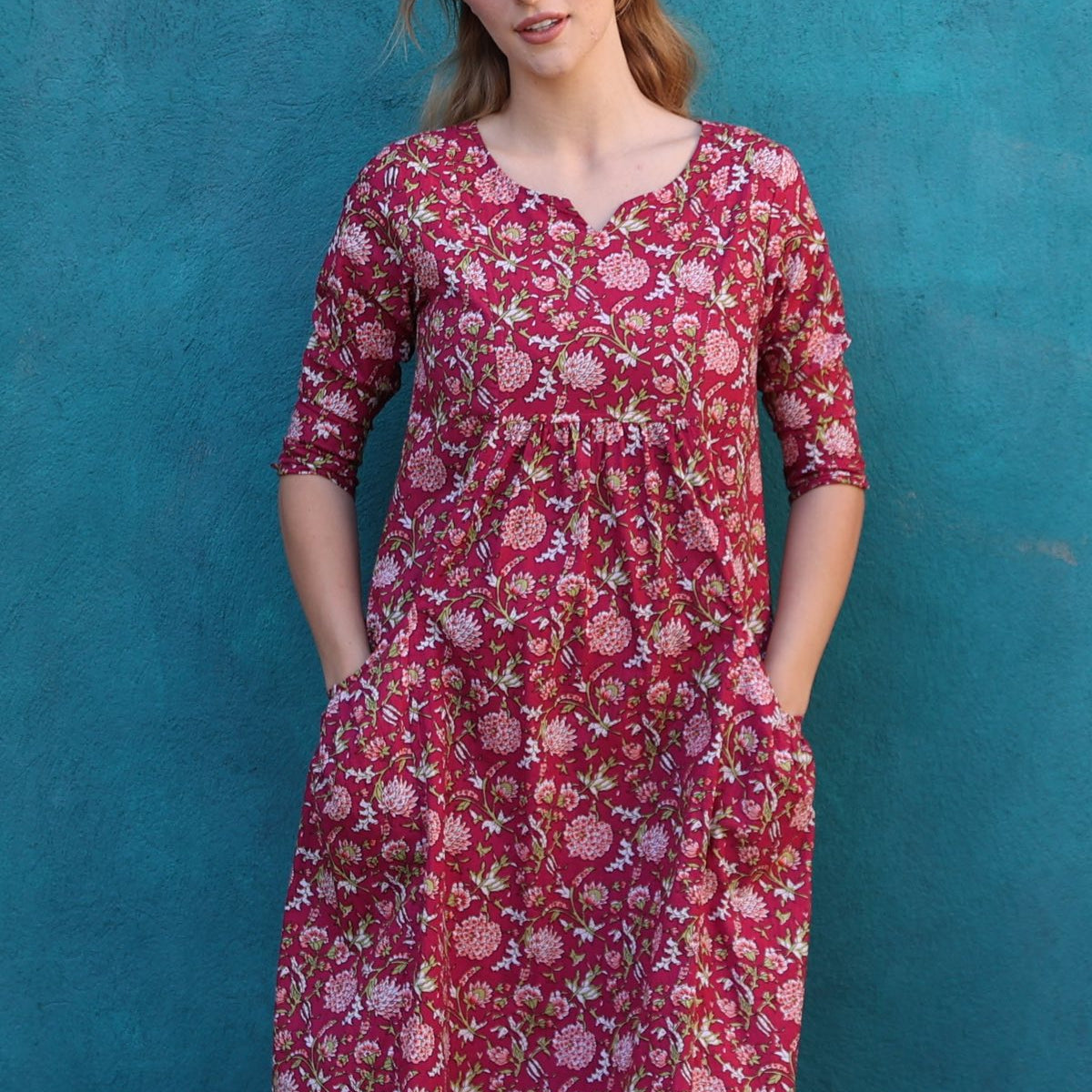 Model wearing 100% cotton dress with beautiful floral print in pink, green and white on bright red base.