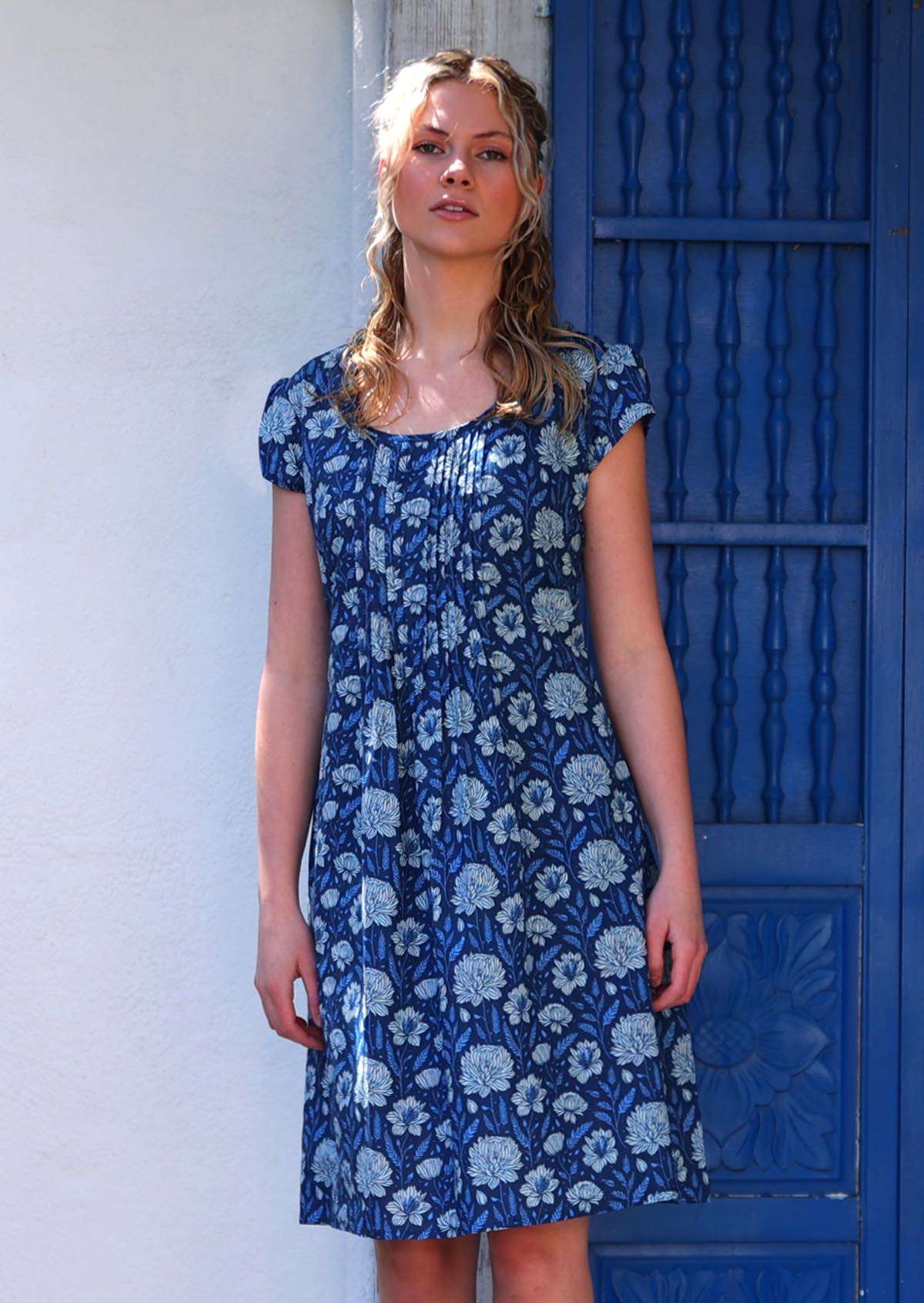 Model wears short sleeved cotton dress with pin tucks across front of bodice in blue floral print
