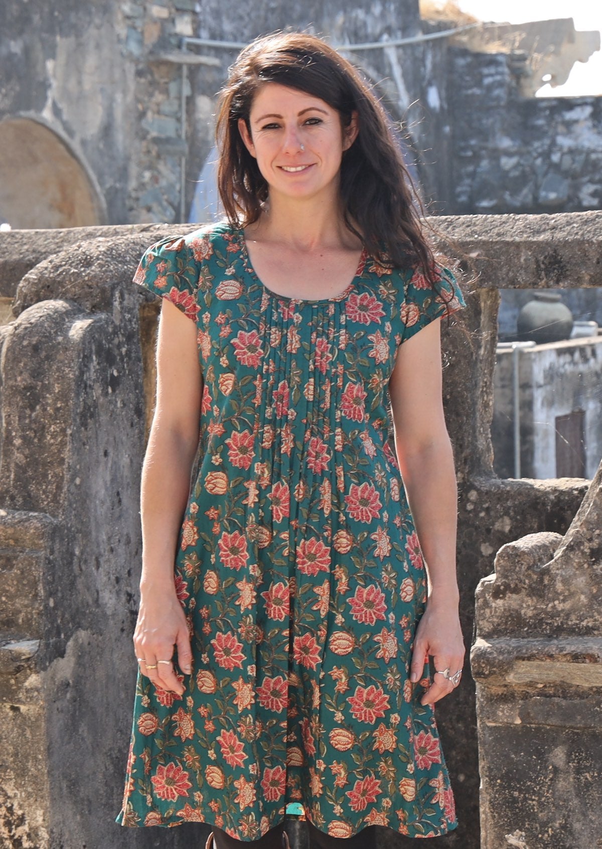 Women with black hairs wearing a knee length cotton dress in green based floral print.