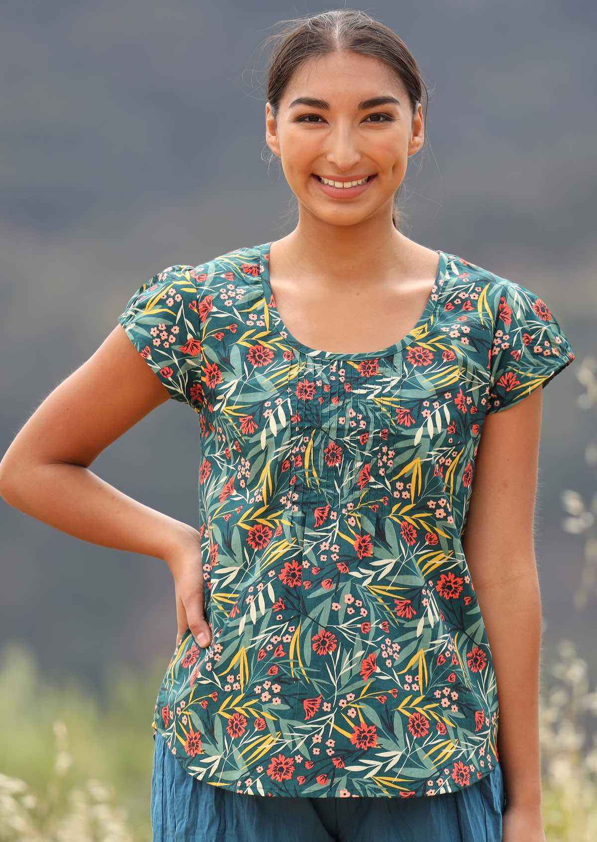 Smiling model wears cotton top with pleats at the neckline. 