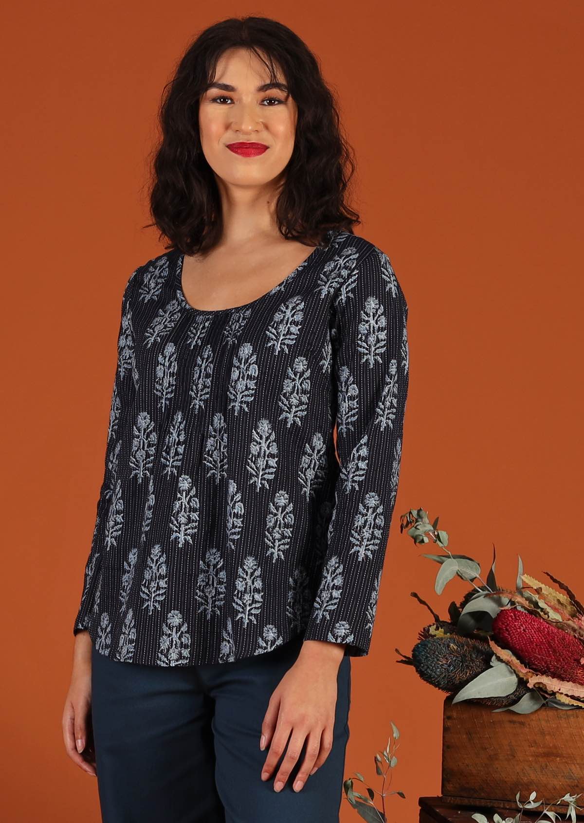  Model in blouse with floral motif and scoop neck worn over blue cotton pants