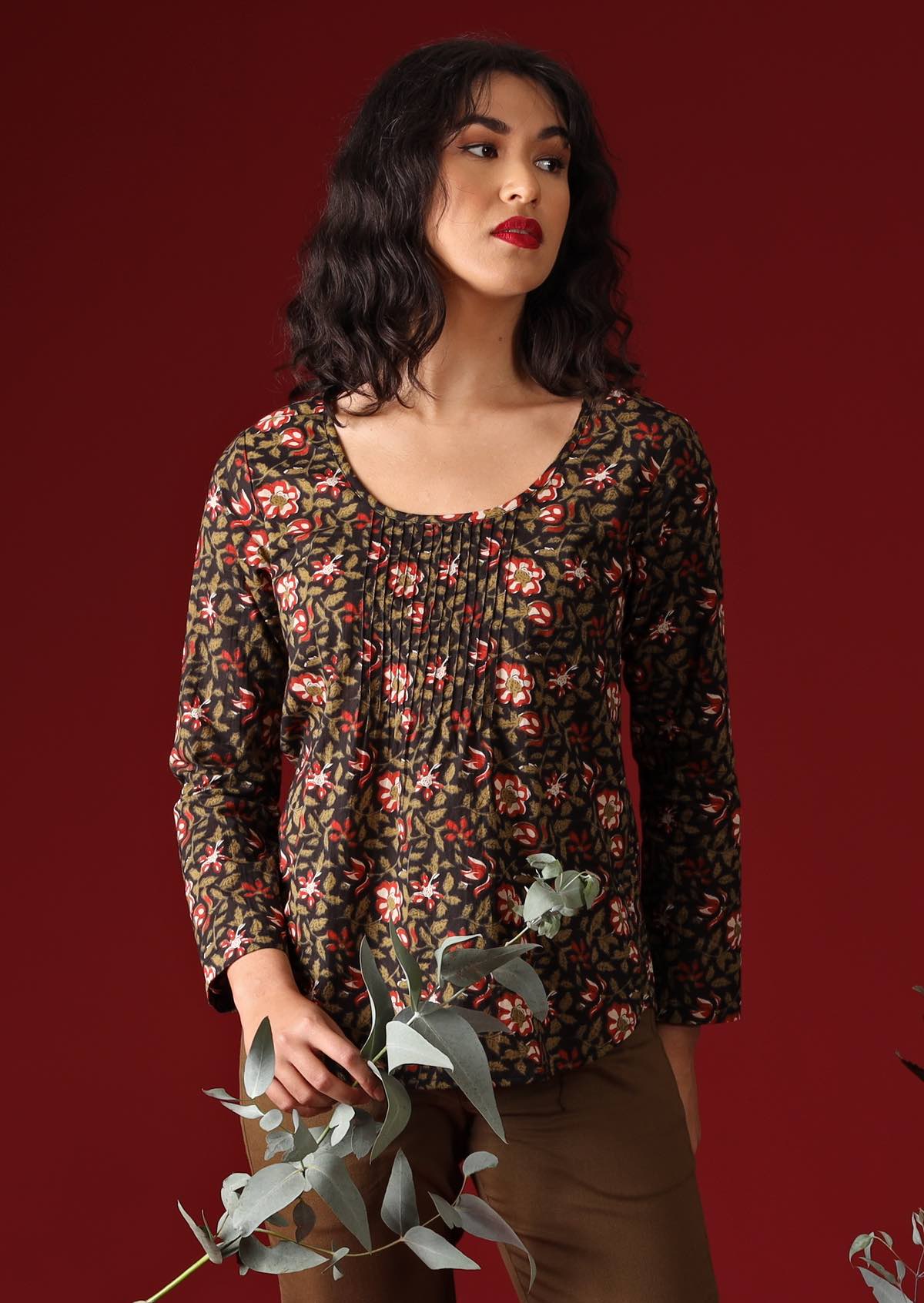 Model with dark hair wearing long sleeve scoop neck cotton women's blouse and holds gum leaves in her hand