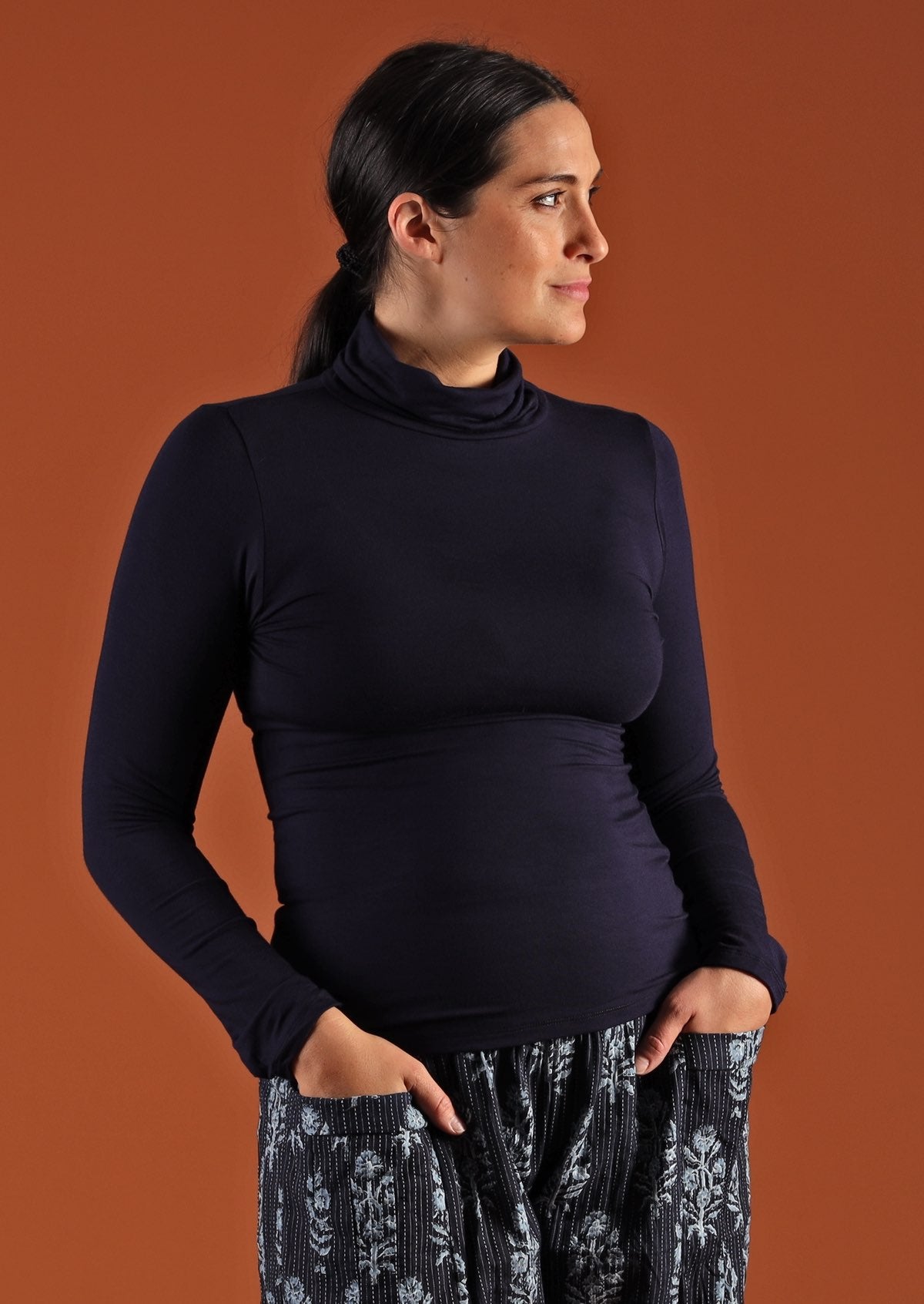 Woman wearing a turtle neck navy blue fitted long sleeve soft stretch rayon top in front of orange wall.