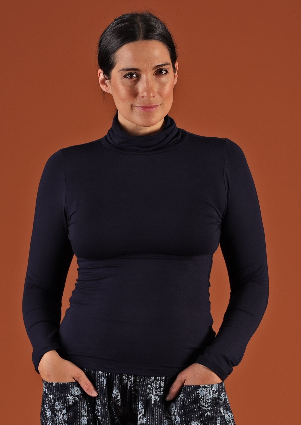 Woman with dark hair wearing a turtle neck navy blue fitted long sleeve soft stretch rayon top.