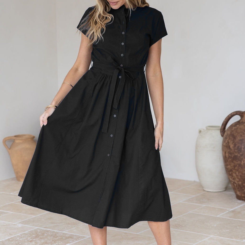Woman wearing a 50's style black cotton button through dress, holding the skirt out to the side