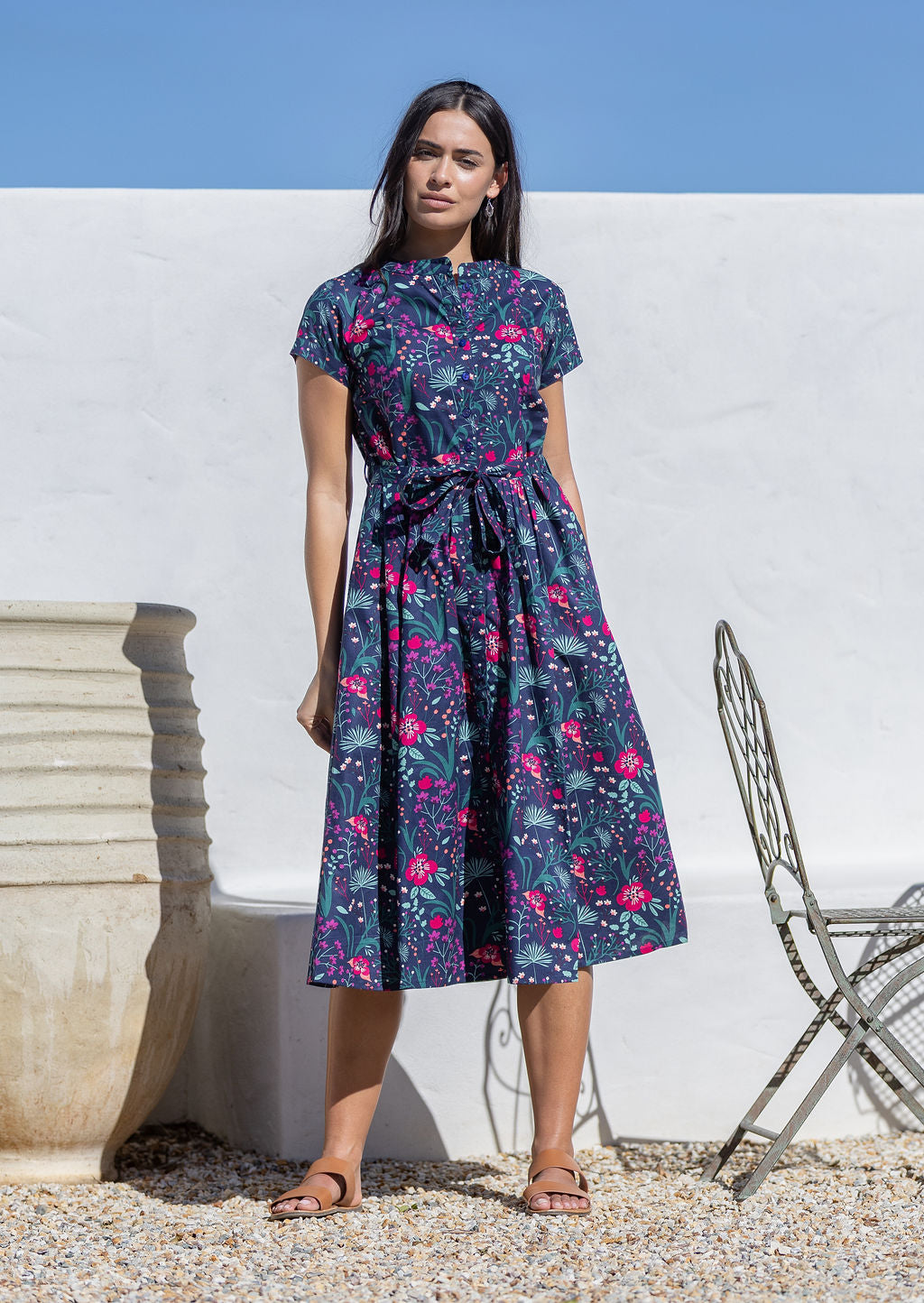 Woman wearing a cotton floral sundress standing outdoors against a white wall.