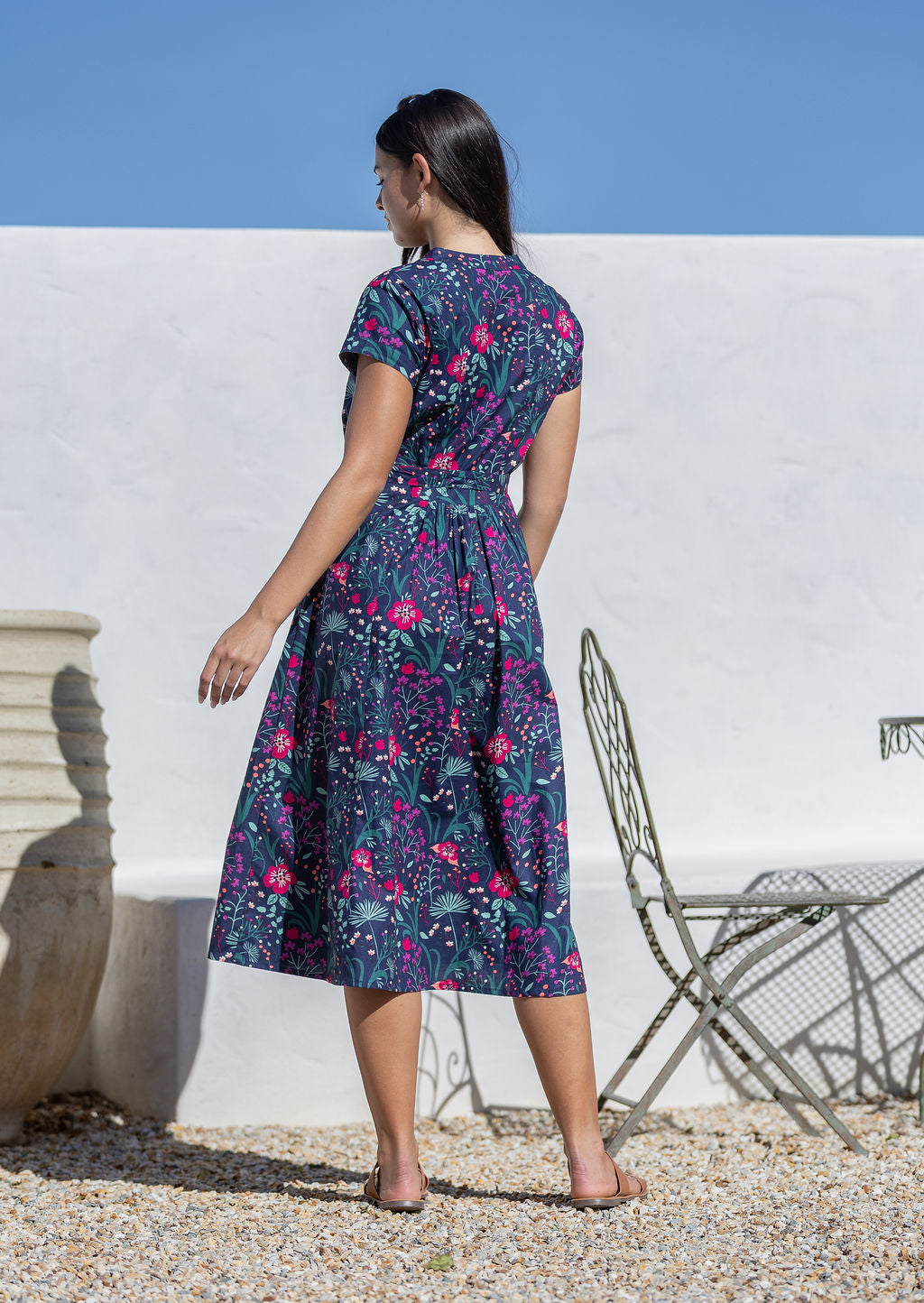 Woman wearing a floral cotton sundress standing outdoors against a white wall.