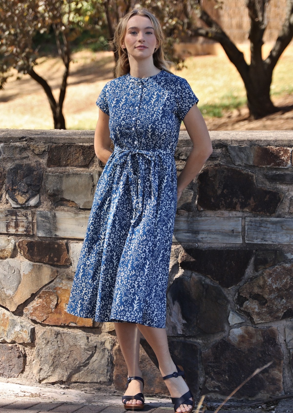 Model poses in cotton 50's style button through dress with high round neckline, cap sleeves and waist tie